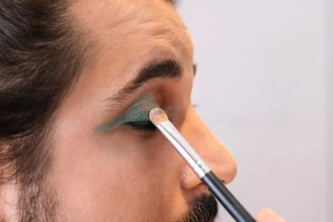 Close-up of a young man applying eye make-up in the bathroom. Using green eye Stock Photos