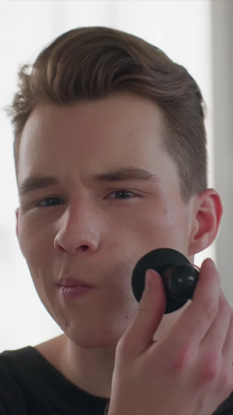 Close up of young man applying makeup to face using black sponge in well lit Stock Footage 343088841