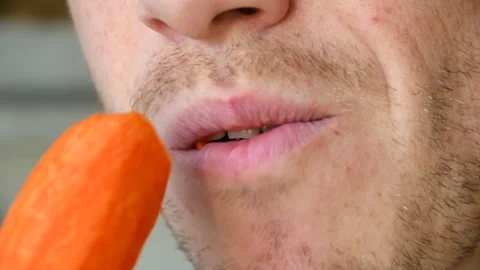 Close up of a young man biting and chewing a fresh carrot 스톡 동영상 337828956