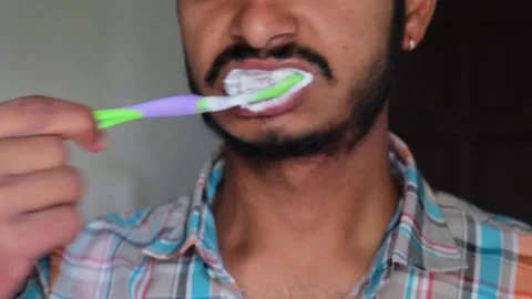 Close-up of a young man brushing his teeth with a green and purple toothbrush Stockbeeldmateriaal 330179674