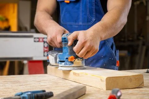 Close up of an young man builder carpenter equals polishes wooden board with  Stock Photos