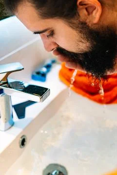 Close-up of a young man with bushy beard, washing his face in the bathroom sink Stock Photos