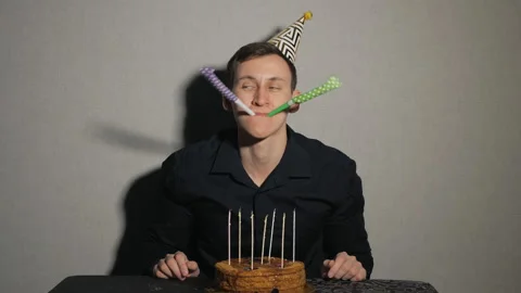 Close up of young man with cake and a candles playing with party blowers Stock Footage 101283869