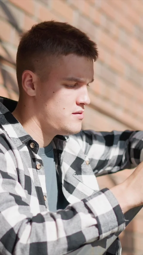 Close up of young man in checkered shirt with brick wall background under soft Stock Footage 345051489