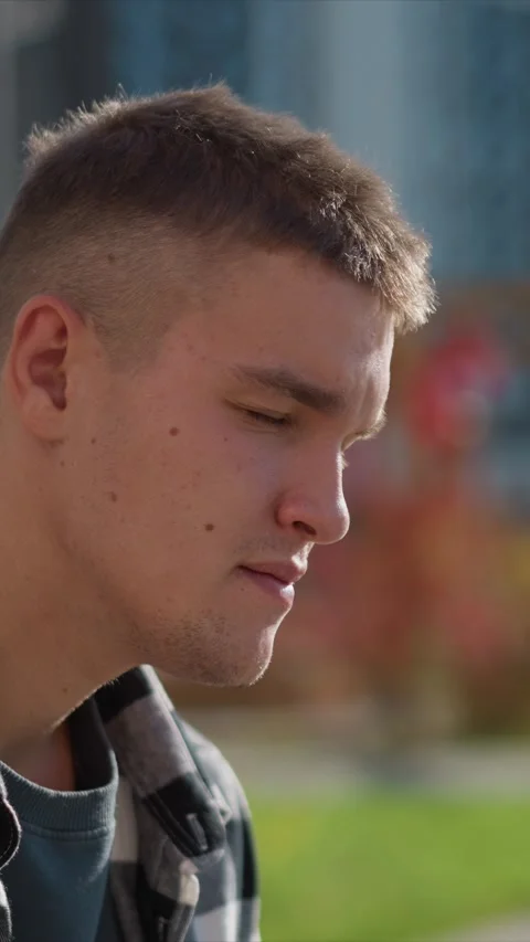 Close up of young man in checkered shirt looking downward outdoors with soft Stock Footage 345052060