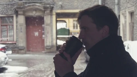 Close-up of young man in coat drinking coffee from plastic cup on snowy street Stock Footage 74896394