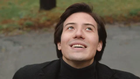 Close-up of a young man in a coat, exposing his face to the rain and holding his Stock Footage 262620634