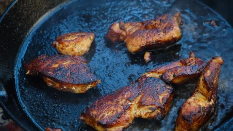 Close up of young man cooking chicken fillet in frying pan at nature Stock Footage 309028752
