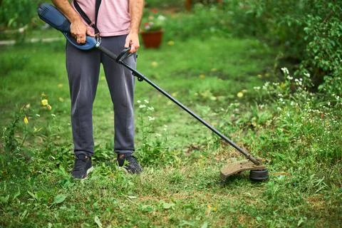 Close up of young man cutting grass with weed cutter on his grassy lawn. Stock Photos