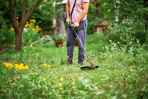 Close up of young man cutting grass with weed cutter on his grassy lawn. Stock-Fotos