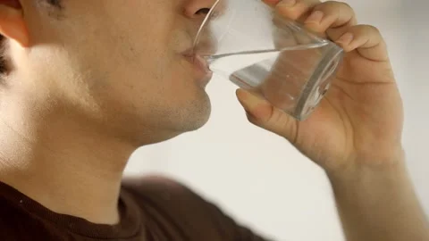 Close-up of a young man drinking a glass of purified water, refreshing himself. 動画素材 320198410