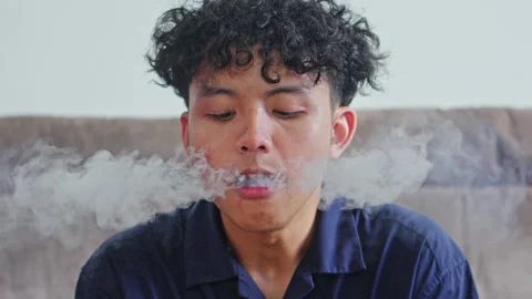Close-up of Young man exhales thick smoke ring while vaping indoors Stock Footage 332388977