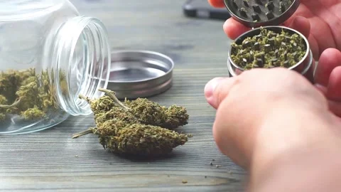 Close up of young man grinding Marijuana buds from jar on wooden table Stock Footage 147164057