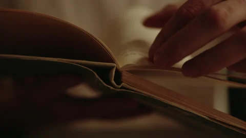 Close-up of young man hand turning page of old antique book in warm light at Stock Footage 312330205