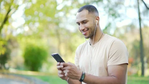 Close up Young man in headphones browsing and typing on his smartphone while  Stock Footage 234875093