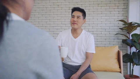 Close up young man holding a cup of drink while sitting on the couch while talki Stock Footage 147366850
