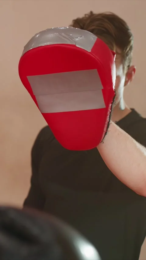 Close up of young man holding red boxing pad while woman punches repeatedly in Stock Footage 343091855