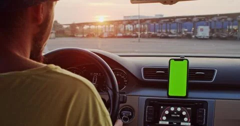 Close-up young man inside car using mounted smartphone navigator on greenscreen Stock Photos