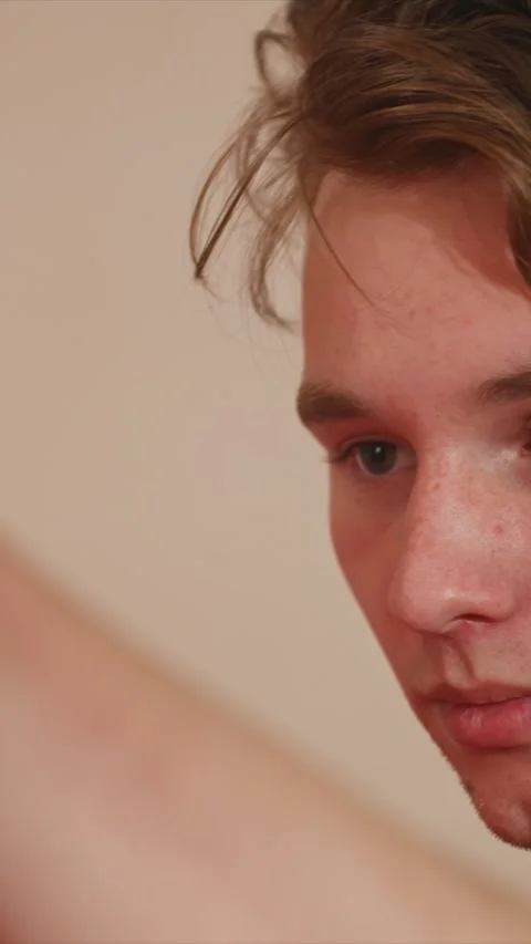 Close up of young man with light brown messy hair and freckles against plain Stock Footage 345549068