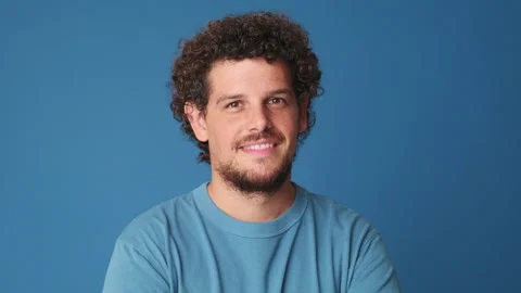Close up, young man looking at the camera with smile isolated on blue background Stock Footage 252031048
