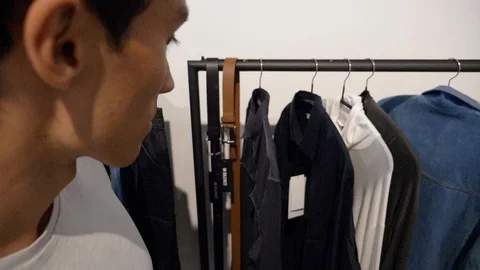 Close-up of young man looking at clothes in clothes store in slow motion 스톡 동영상 114874616