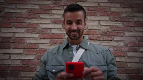 Close up young man looking smiling camera while holding red cell phone leaning Stock Footage 274912766