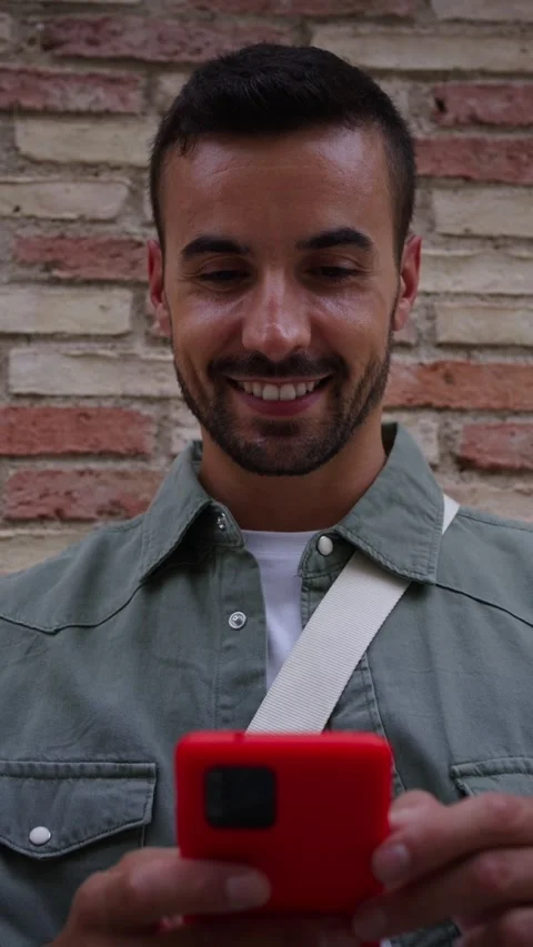 Close up young man looking smiling camera while holding red cell phone leaning Stock Footage 275621244