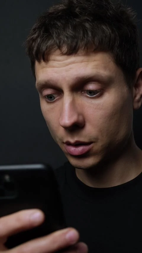 Close-up of young man looking surprised at smartphone on black background Stock Footage 318066755