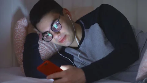 Close-up of a young man lying in bed with headphones, browsing the Internet at Stock Footage 159879081