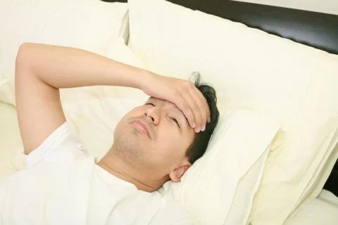 Close up of young man lying down in bed taking temperature and having flu Stock Photos