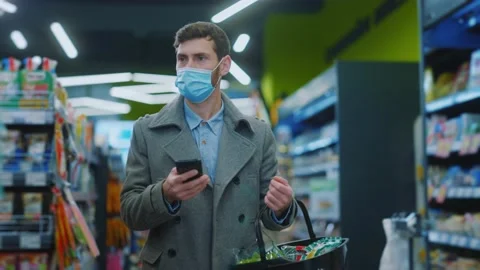 Close up young man in mask walking looking on shopping list in phone hold a cart Stock Footage 143739107