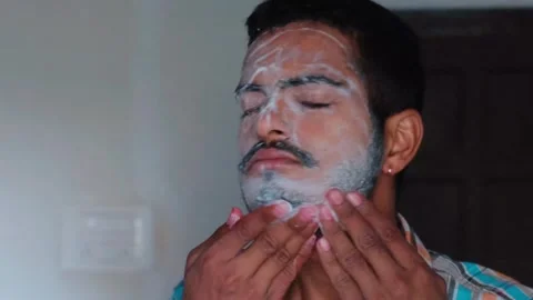 Close-up of a young man massaging white shaving cream or face wash on his face Stockbeeldmateriaal 330179631