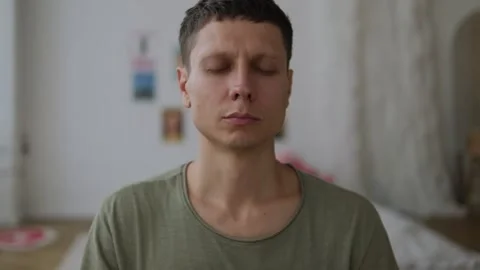 Close-up of young man meditating with closed eyes in bedroom, embracing the Stock Footage 311048455