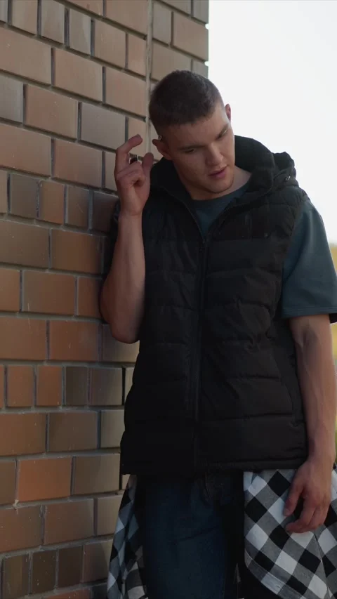 Close up young man near brick wall lighting cigarette wearing vest t shirt Stock Footage 345066539