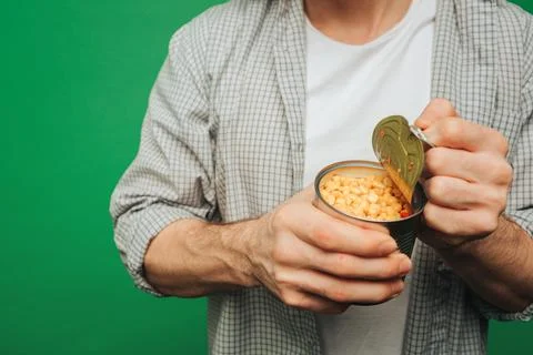 Close up young man opens corn in a jar, isolated on green background Stock Photos