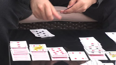 Close-up of a young man playing cards solitaire on a table with his hands in the Stock Footage 155795069