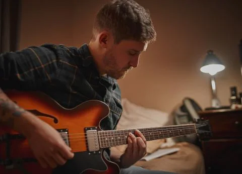 Close-up of a young man practicing playing guitar at evening in his home Stock Photos