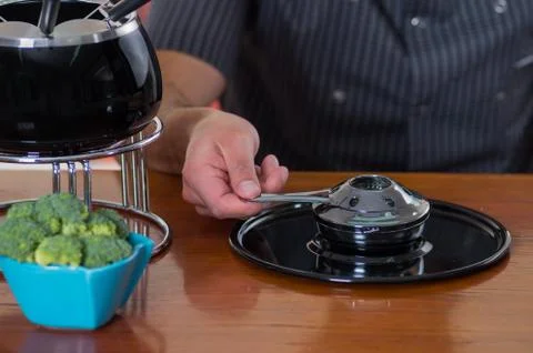 Close up of a young man preparing the machine for a gourmet Swiss fondue dinner 스톡 사진