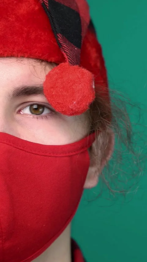 Close-up of a young man in a red Santa hat with pompom and red cloth mask  Stock Footage 345691717