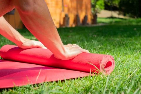 Close up of young man rolling his yoga mat in the garden on the grass. Peacef Stock Photos