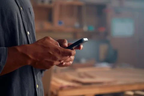 Close-up of young man in shirt using mobile phone by woodpile in woodworking Stock Photos