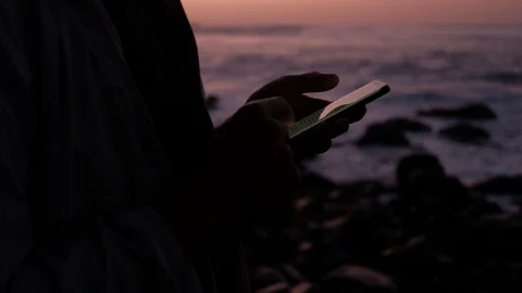 Close up of young man silhouette scrolling and using his smartphone in last Stock Footage 123689111