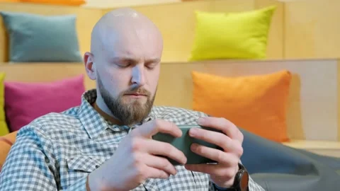 Close up of an young man sits on a bean bag while playing online using his phone Video stock 153109754
