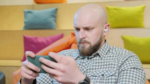 Close up of an young man sits on a bean bag while playing online using his phone Stock Footage 153616418
