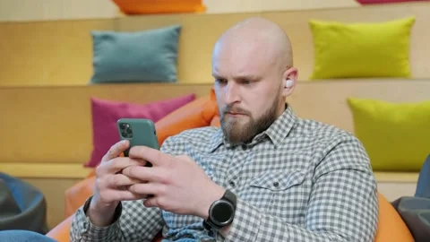 Close up of an young man sits on a bean bag while playing online using his phone Stock Footage 155810684