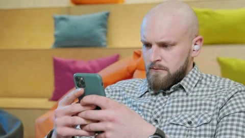 Close up of an young man sits on a bean bag while playing online using his phone Stock Footage 156338552
