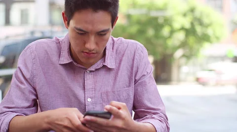 Close up of a young man sitting outside using his cell phone and smiling Vídeo Stock 57512625