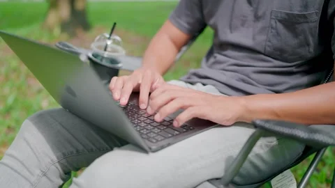 Close-up of a young man sitting in a work chair on a laptop in nature. Stock Footage 283186458