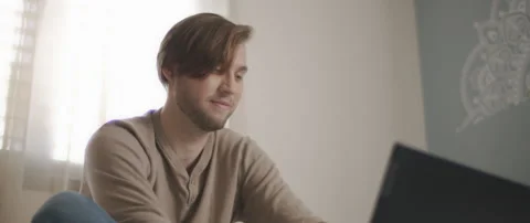 A close up of a young man smiling while sitting in bed and working on a compu Stock Footage 135095485