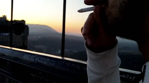 Close up of young man smoking a cigarette walking across the bridge in sunset 스톡 동영상 144014504